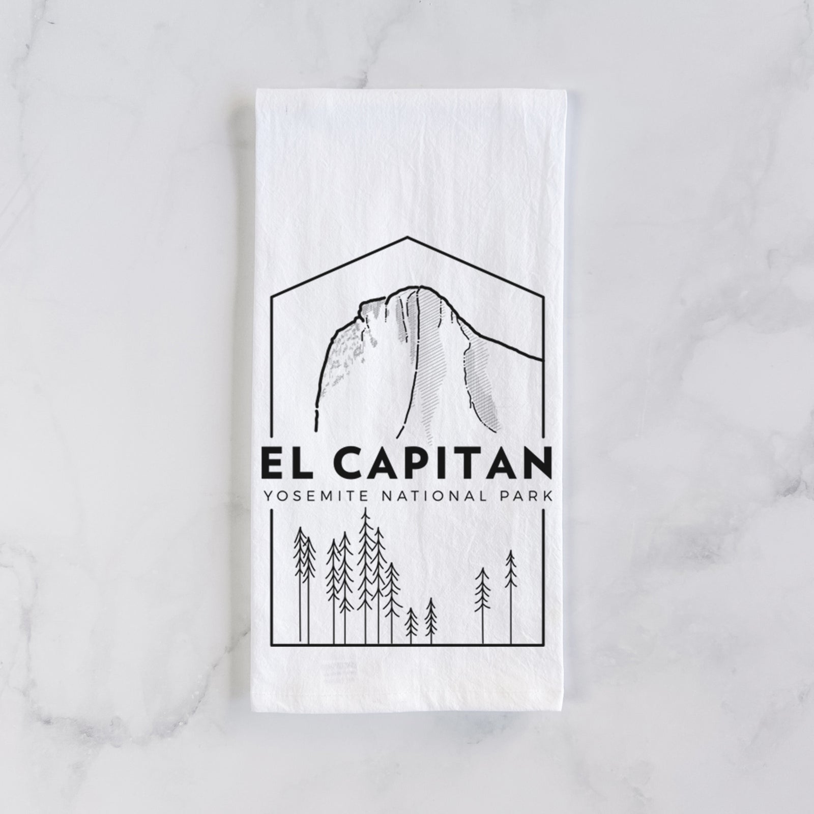 White cotton tea towel printed with a black line art badge of El Capitan rising above a pine forest, with the words El Capitan, Yosemite National Park, on a marble counter beside a round wooden cutting board and greenery.
