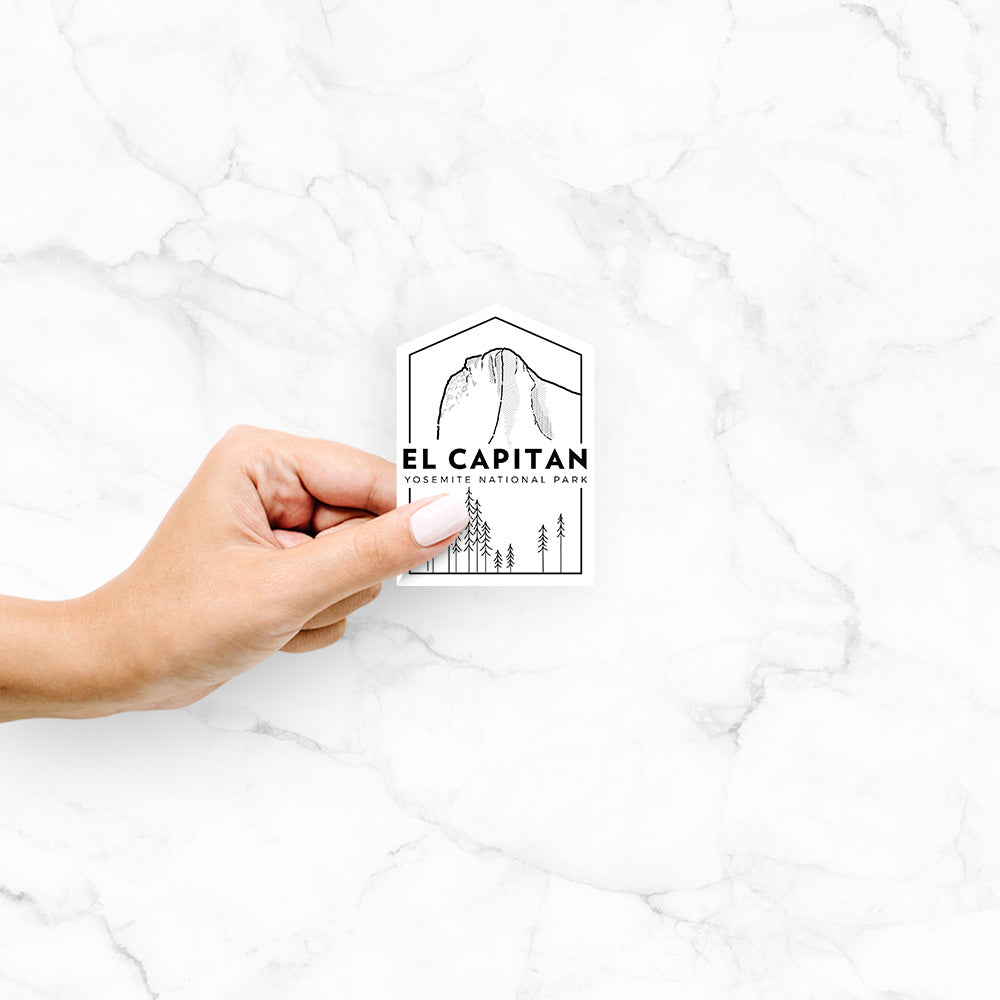 Hand holding a 4 inch vinyl decal of a black line art badge of El Capitan rising above a pine forest, with the words El Capitan, Yosemite National Park.