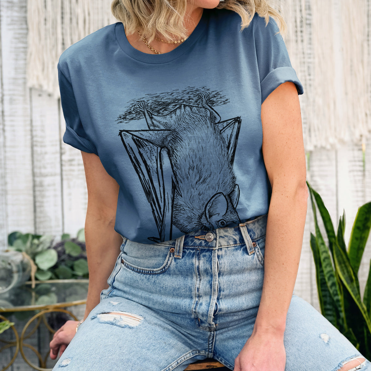 Woman wearing a steel blue lightweight cotton t-shirt printed with a detailed black ink illustration of a big brown bat hanging upside down.