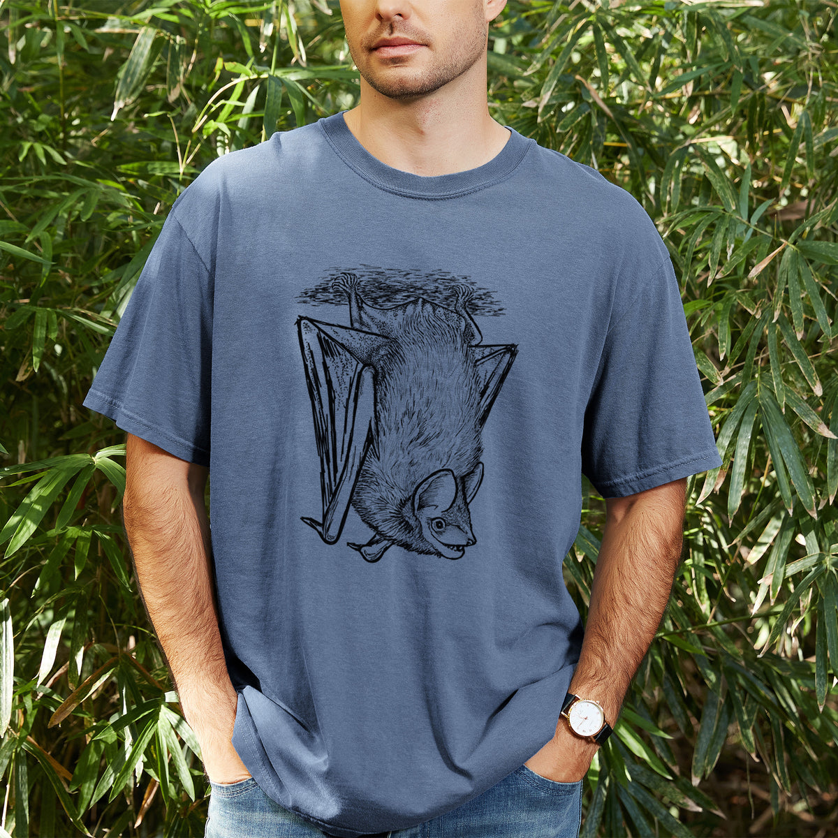 Man wearing a Comfort Colors t-shirt printed with a detailed black ink illustration of a big brown bat hanging upside down, outdoors.