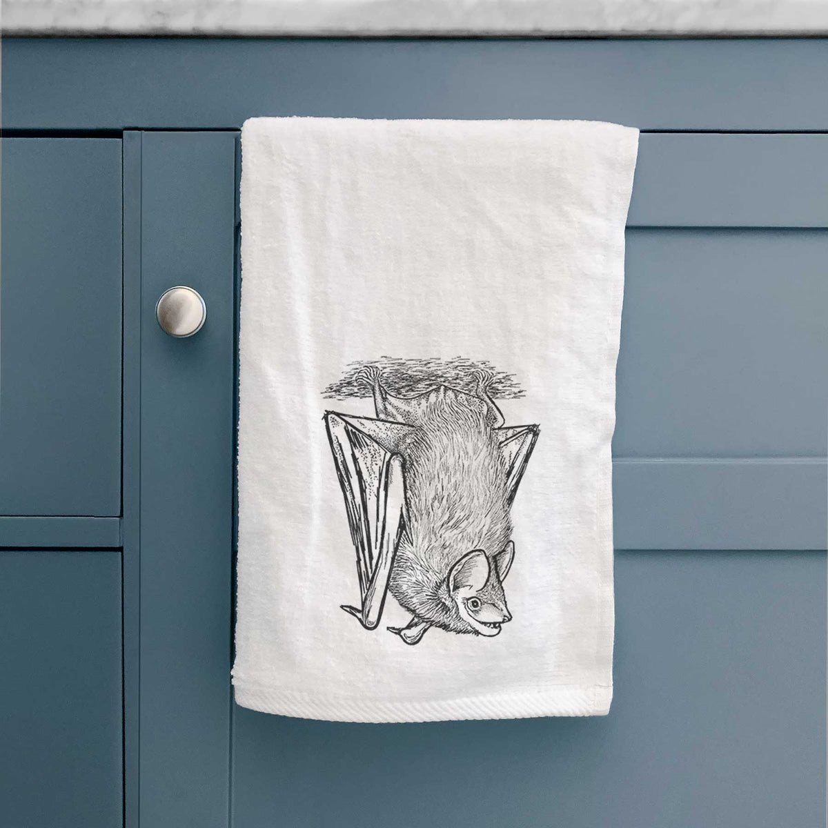White hand towel printed with a detailed black ink illustration of a big brown bat hanging upside down, hanging on a cabinet door.