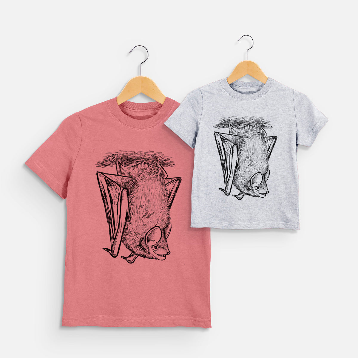 Two youth t-shirts in different colors on hangers, printed with a detailed black ink illustration of a big brown bat hanging upside down.
