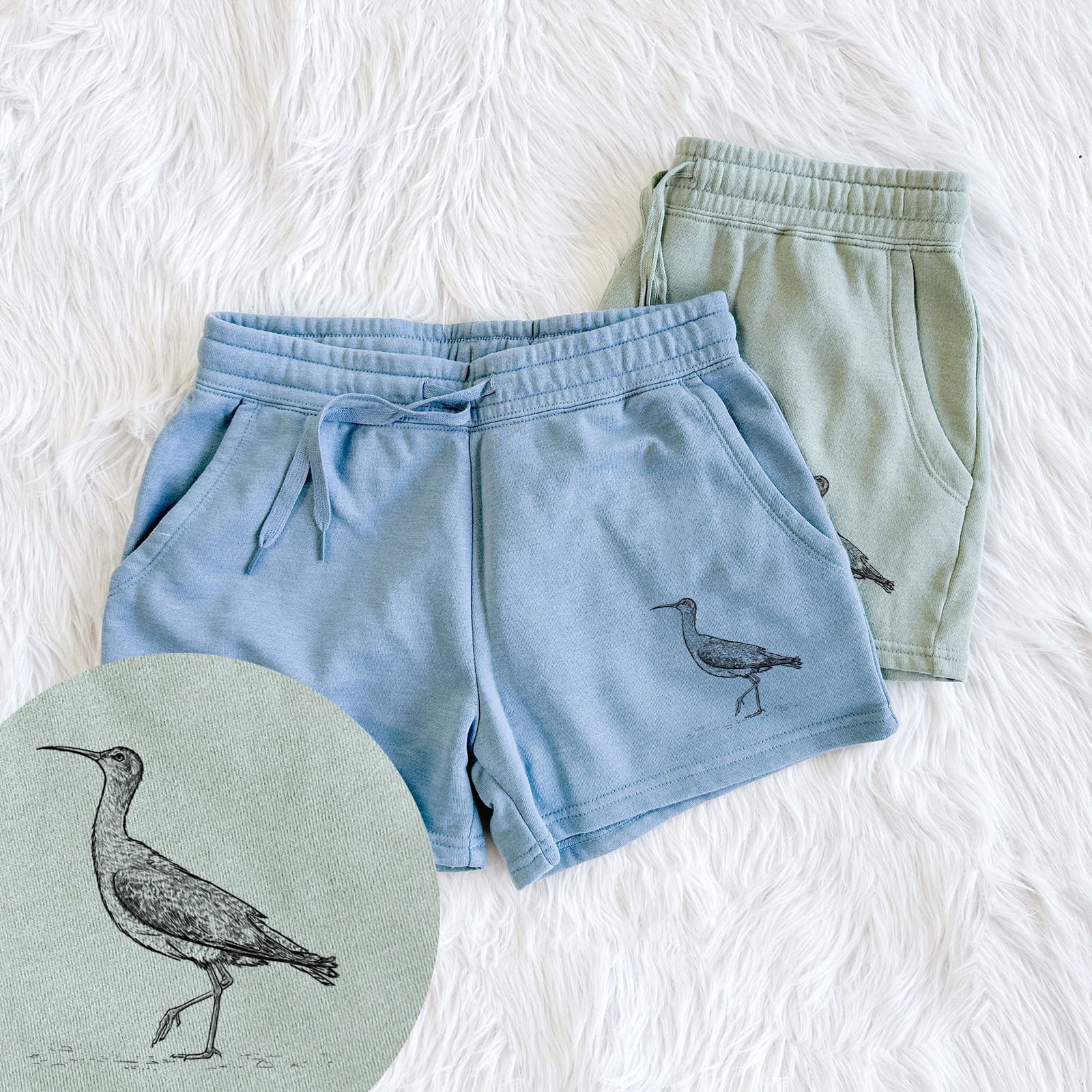 Two pairs of Cali Wave shorts in different colors printed with a detailed black ink illustration of an Eskimo curlew with its long curved bill, walking, with a close-up of the print.