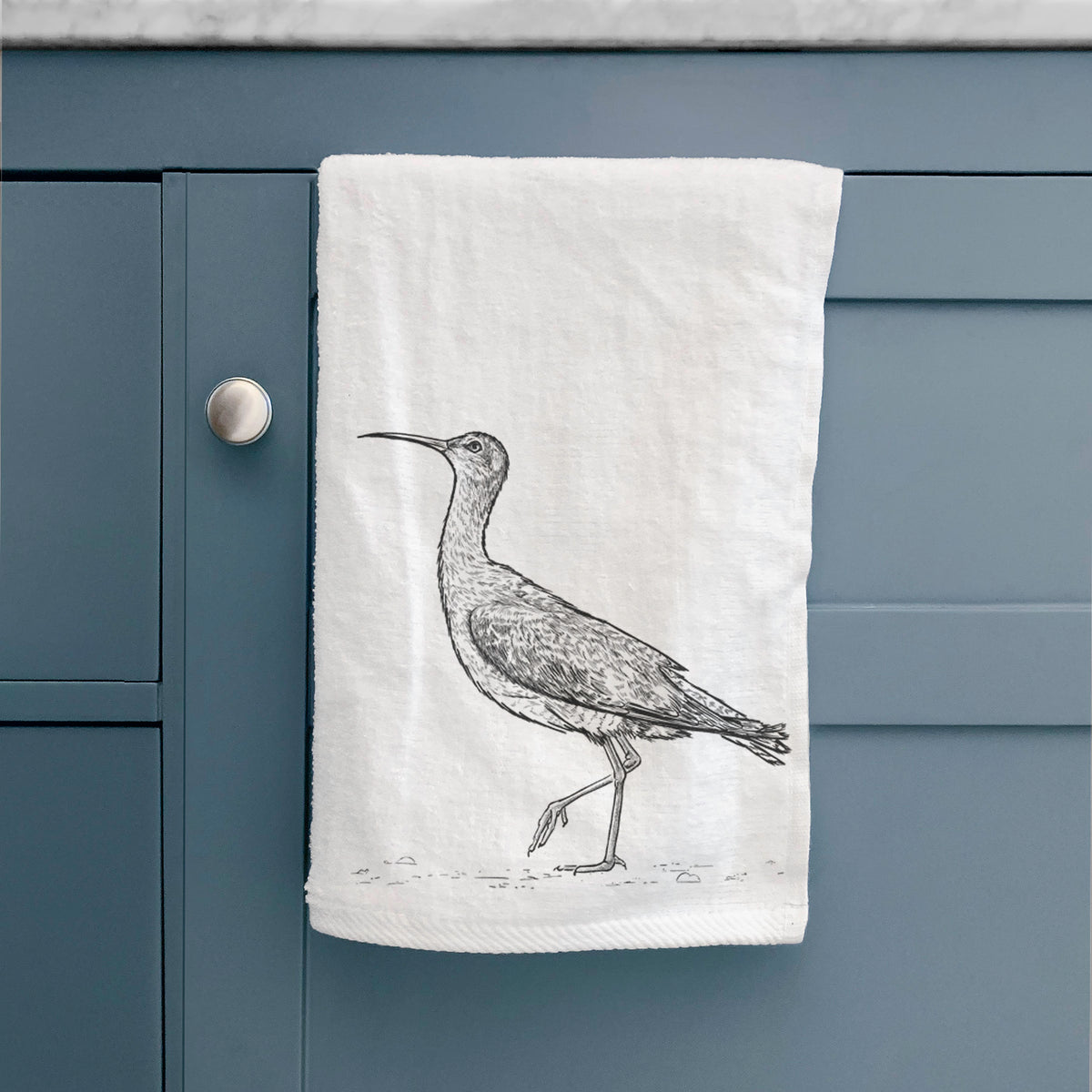 White hand towel printed with a detailed black ink illustration of an Eskimo curlew with its long curved bill, walking, hanging on a cabinet door.