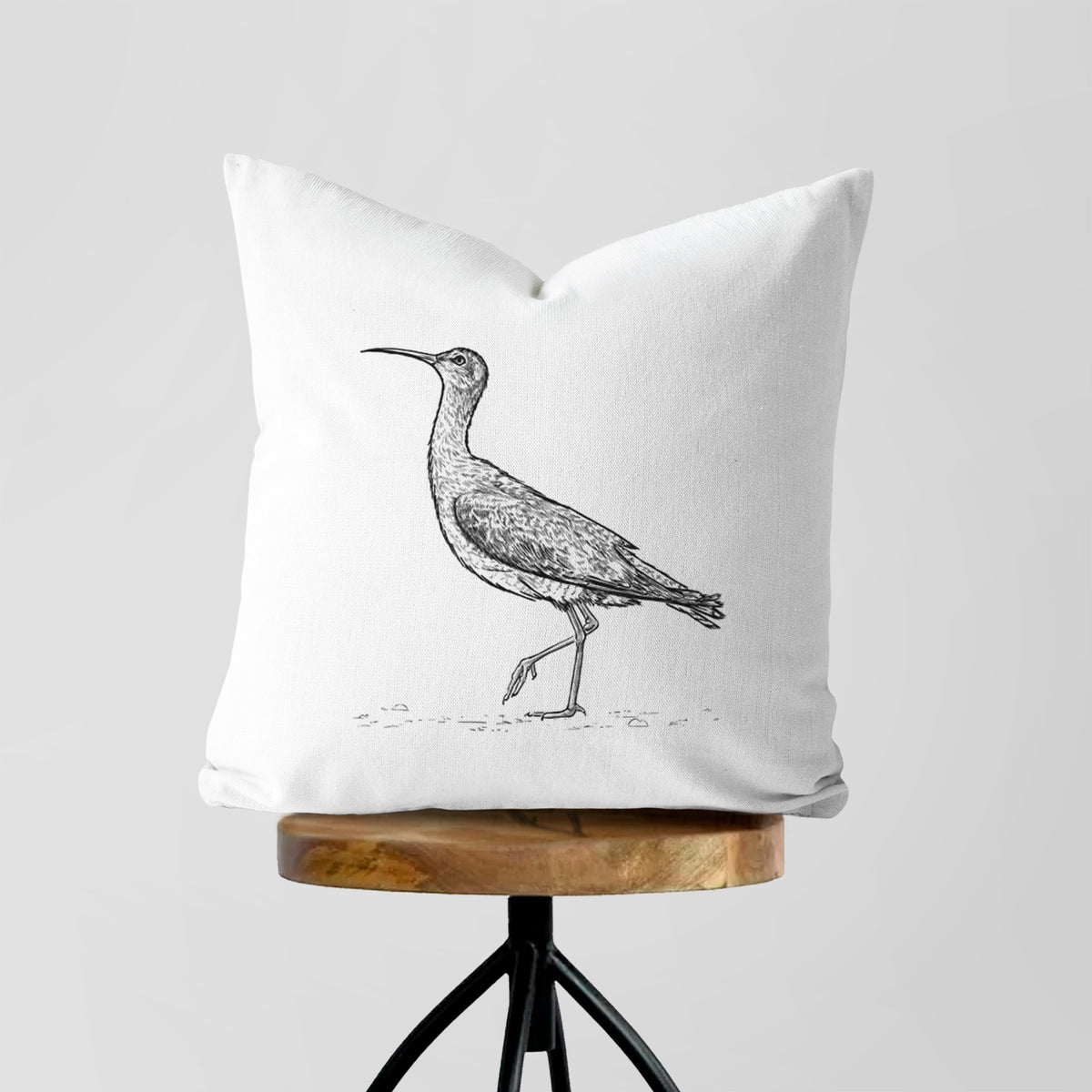 White pillow cover printed with a detailed black ink illustration of an Eskimo curlew with its long curved bill, walking, on a wooden stool.