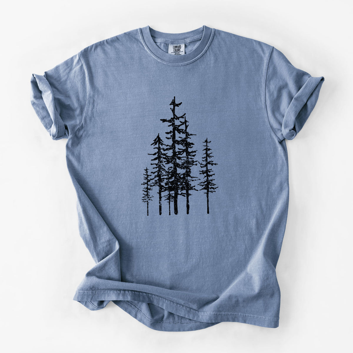Blue jean Comfort Colors t-shirt laid flat, printed with a black ink illustration of a cluster of evergreen trees of varying heights.