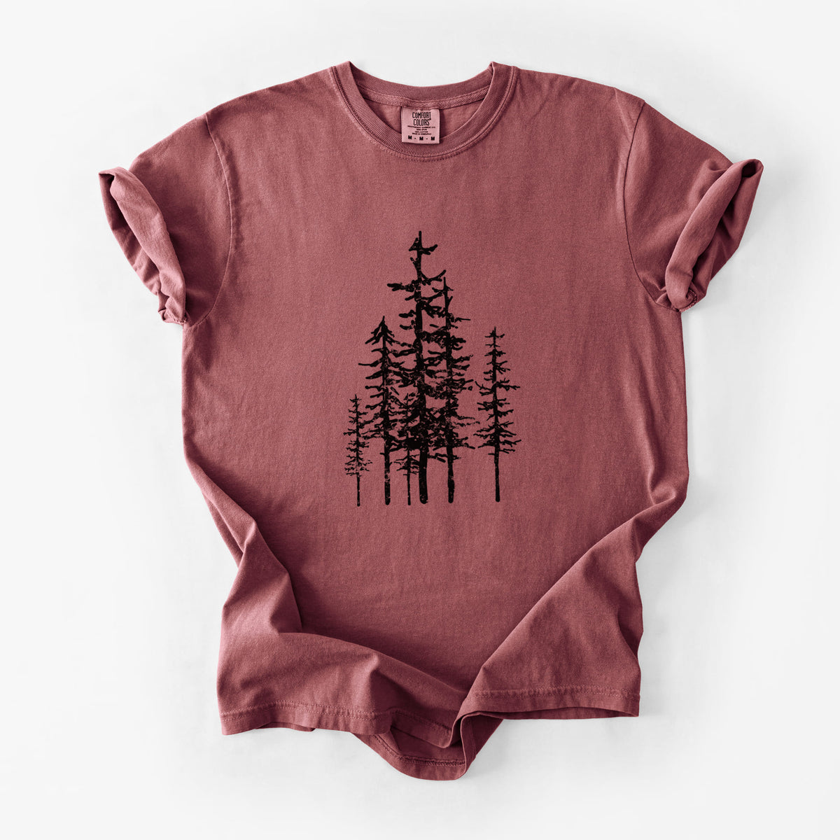 Brick red Comfort Colors t-shirt laid flat, printed with a black ink illustration of a cluster of evergreen trees of varying heights.