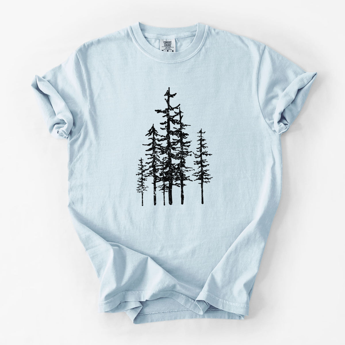 Chambray blue Comfort Colors t-shirt laid flat, printed with a black ink illustration of a cluster of evergreen trees of varying heights.