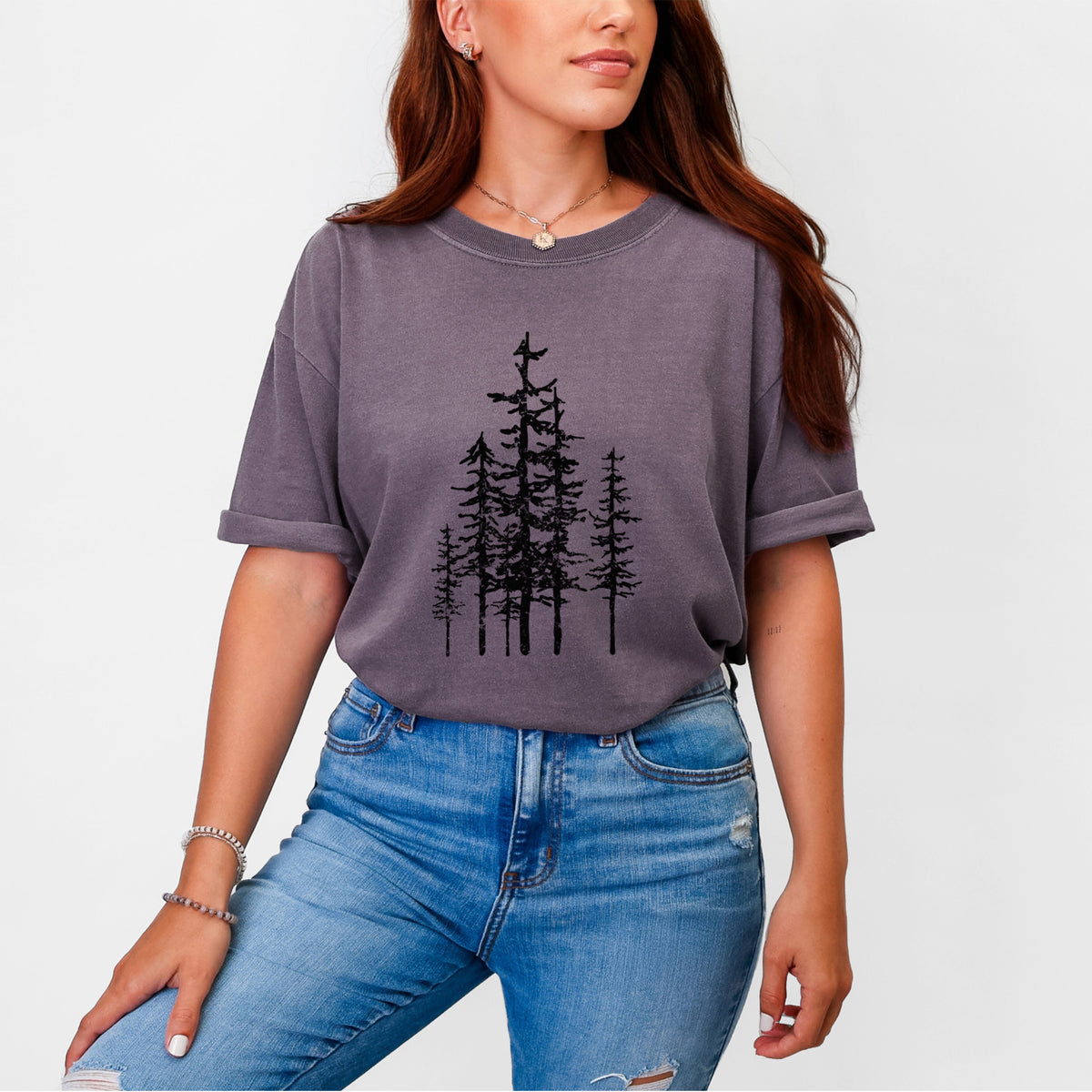 Woman wearing a Comfort Colors t-shirt printed with a black ink illustration of a cluster of evergreen trees of varying heights.