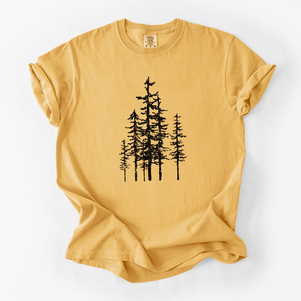 Golden wheat yellow Comfort Colors t-shirt laid flat, printed with a black ink illustration of a cluster of evergreen trees of varying heights.