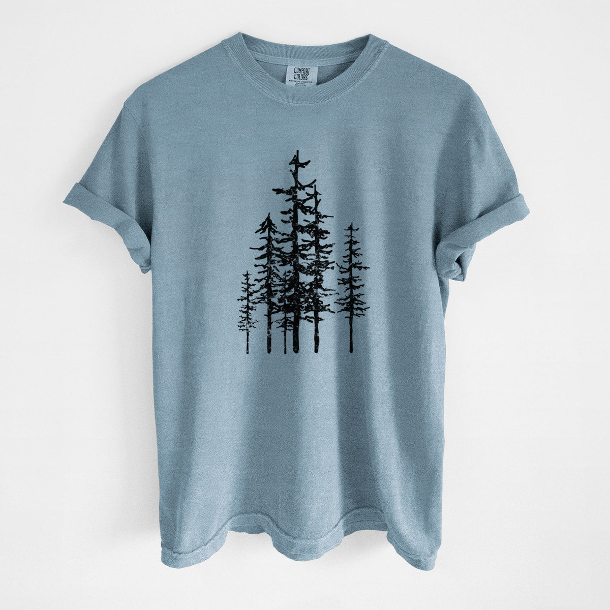 Steel blue Comfort Colors t-shirt laid flat, printed with a black ink illustration of a cluster of evergreen trees of varying heights.