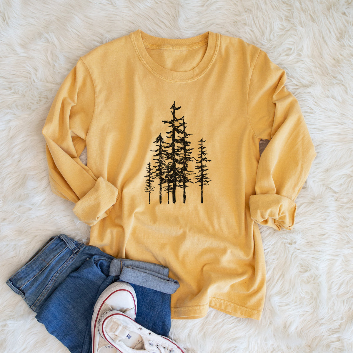 Golden wheat yellow Comfort Colors long sleeve shirt printed with a black ink illustration of a cluster of evergreen trees of varying heights, shown in a lifestyle photo.