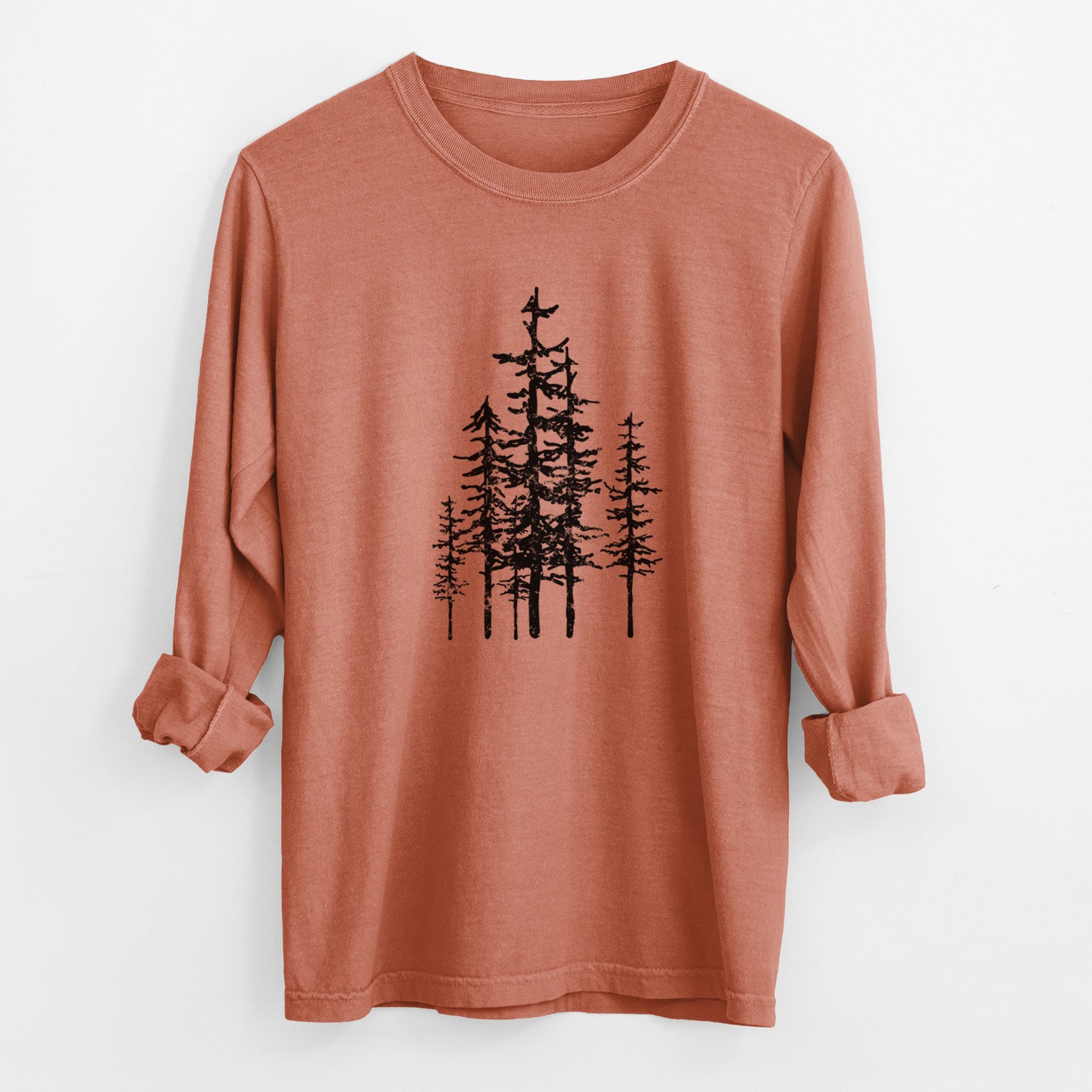 Yam burnt orange Comfort Colors long sleeve shirt laid flat with the cuffs rolled, printed with a black ink illustration of a cluster of evergreen trees of varying heights.