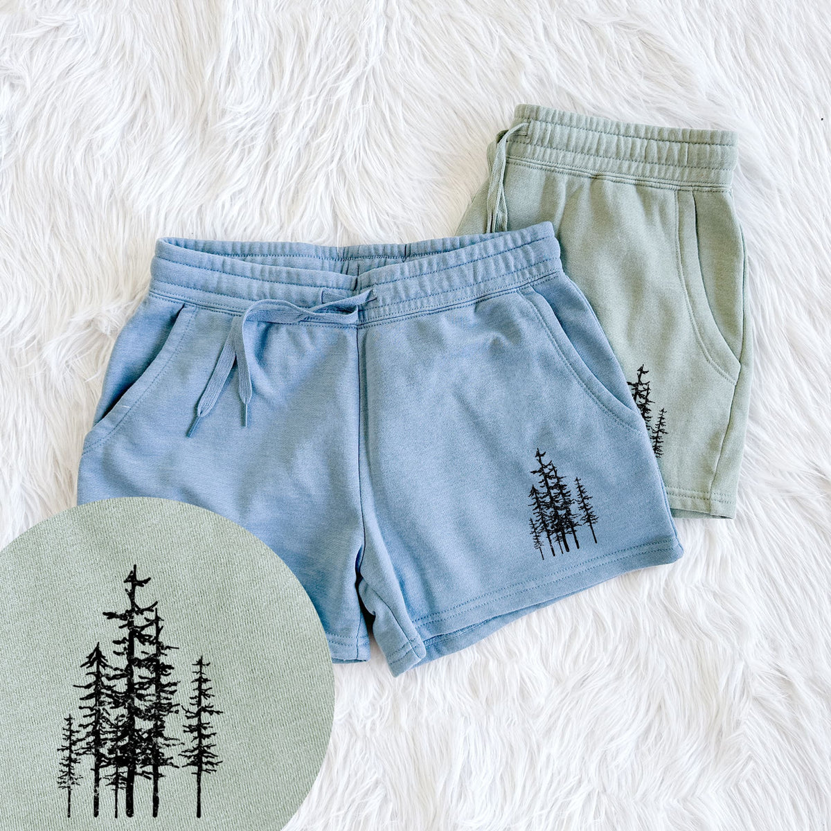 Two pairs of Cali Wave shorts in different colors printed with a black ink illustration of a cluster of evergreen trees of varying heights, with a close-up of the print.