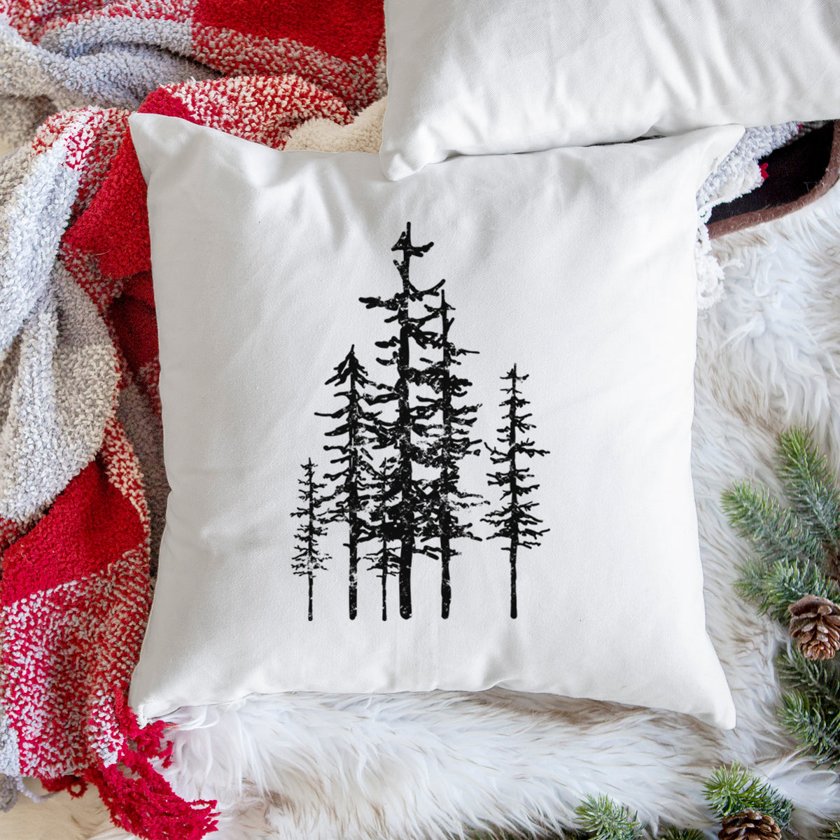 White pillow cover printed with a black ink illustration of a cluster of evergreen trees of varying heights, on a woven chair.