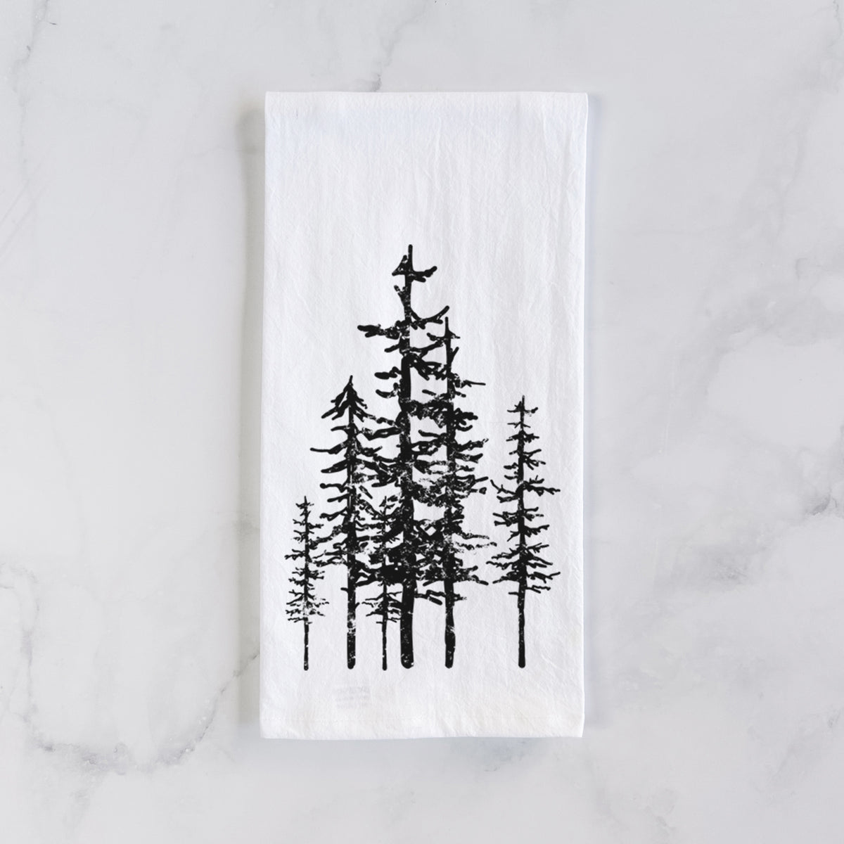 White cotton tea towel laid flat on marble, printed with a black ink illustration of a cluster of evergreen trees of varying heights.