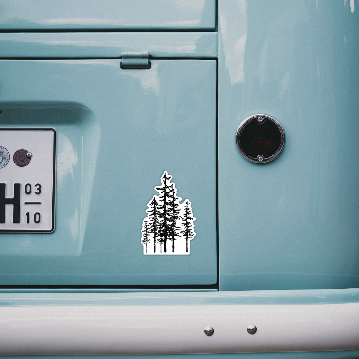 4 inch vinyl decal of a black ink illustration of a cluster of evergreen trees of varying heights on the back of a van.