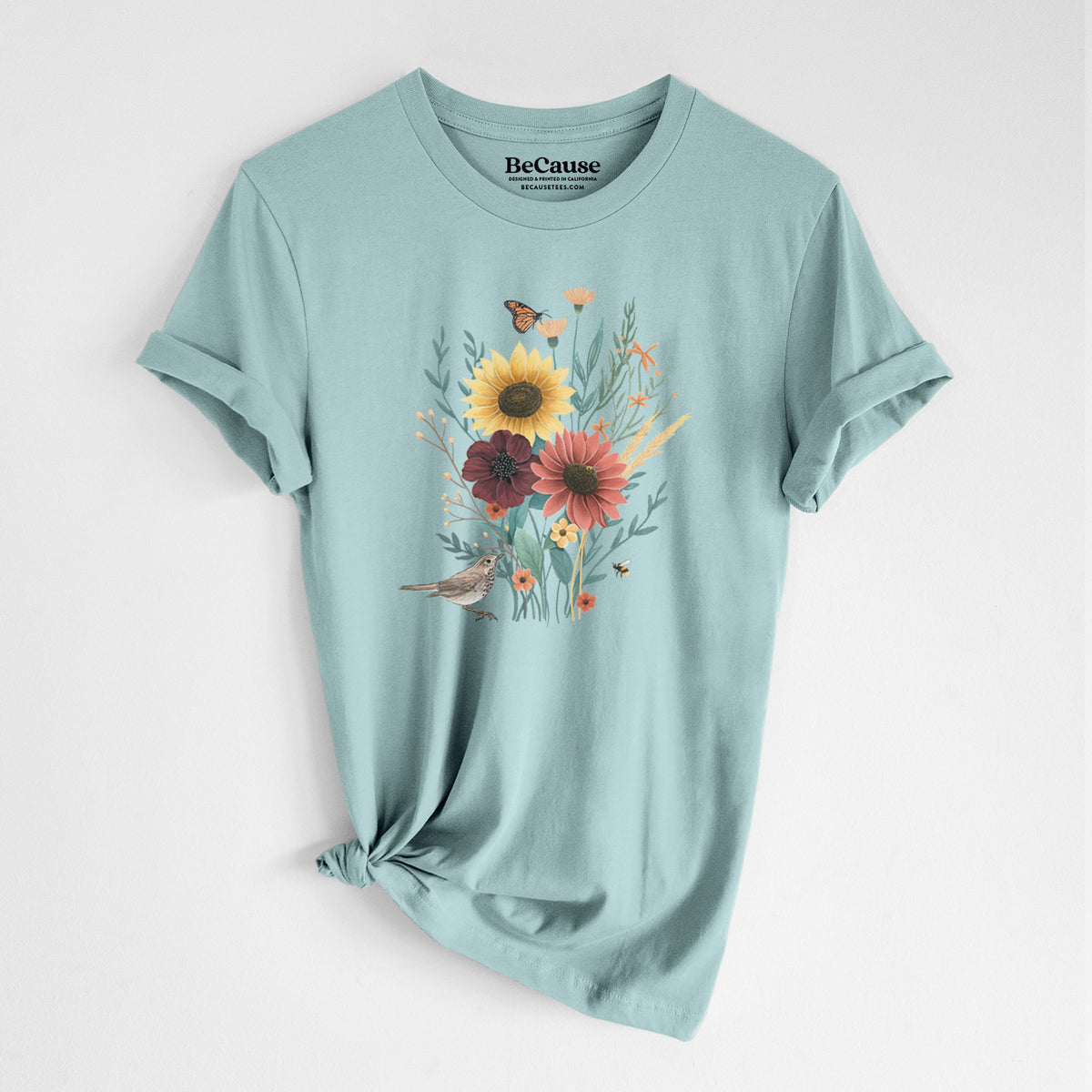 Dusty blue lightweight cotton t-shirt laid flat with the sleeves rolled, printed with a full-color bouquet of sunflowers, red flowers and wildflowers with butterflies and a small bird.
