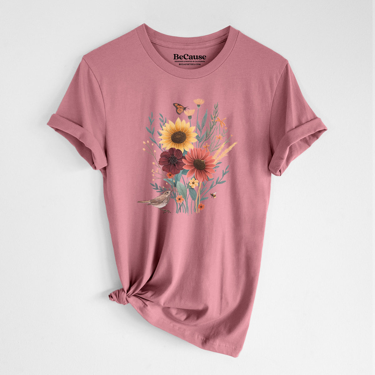 Mauve pink lightweight cotton t-shirt laid flat with the sleeves rolled, printed with a full-color bouquet of sunflowers, red flowers and wildflowers with butterflies and a small bird.