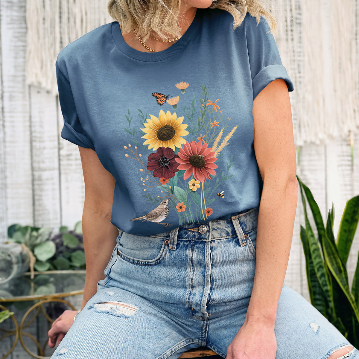 Woman wearing a steel blue lightweight cotton t-shirt printed with a full-color bouquet of sunflowers, red flowers and wildflowers with butterflies and a small bird.