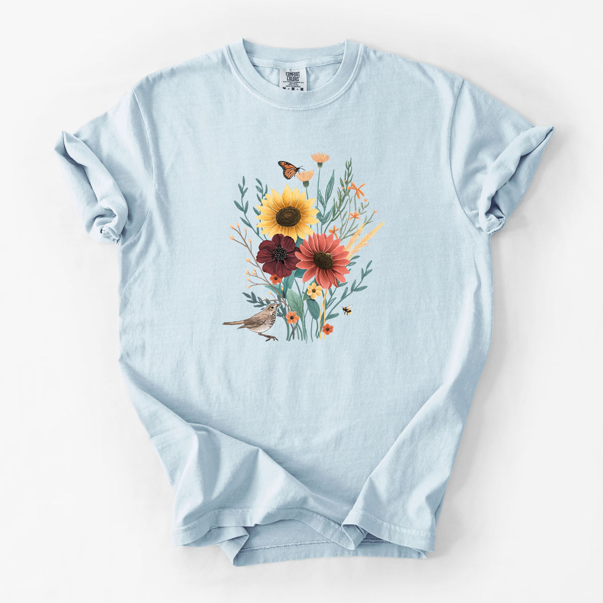 Chambray blue Comfort Colors t-shirt laid flat, printed with a full-color bouquet of sunflowers, red flowers and wildflowers with butterflies and a small bird.