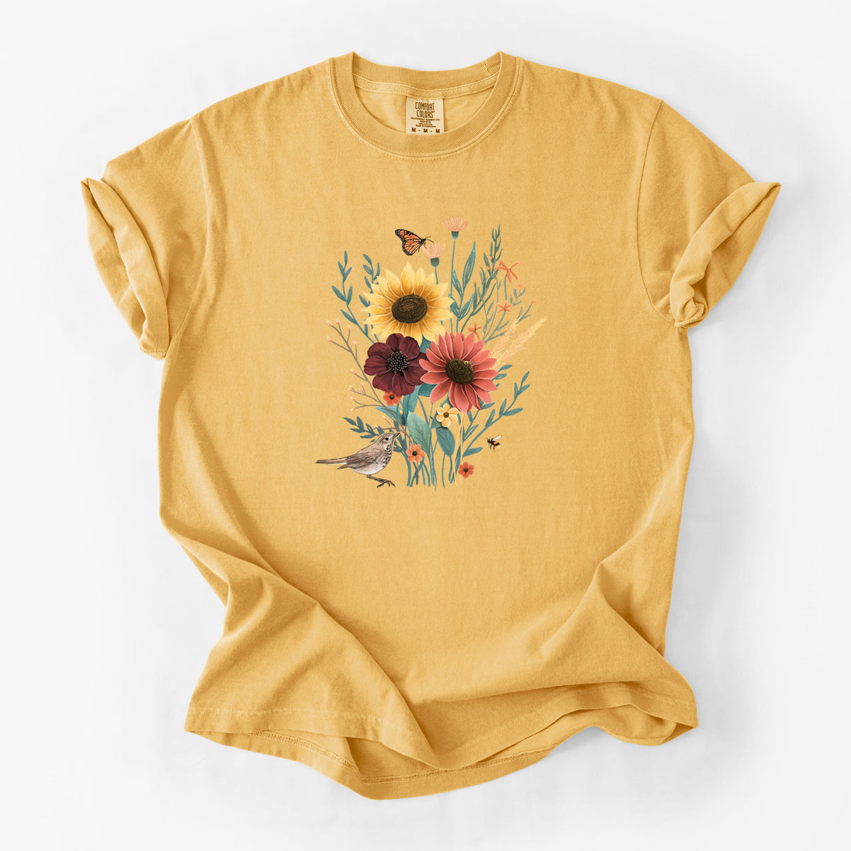 Golden wheat yellow Comfort Colors t-shirt laid flat, printed with a full-color bouquet of sunflowers, red flowers and wildflowers with butterflies and a small bird.