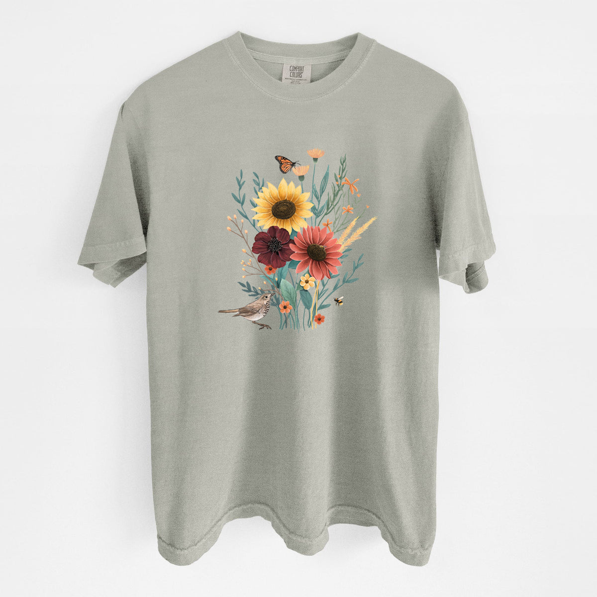 Sandstone beige Comfort Colors t-shirt laid flat, printed with a full-color bouquet of sunflowers, red flowers and wildflowers with butterflies and a small bird.
