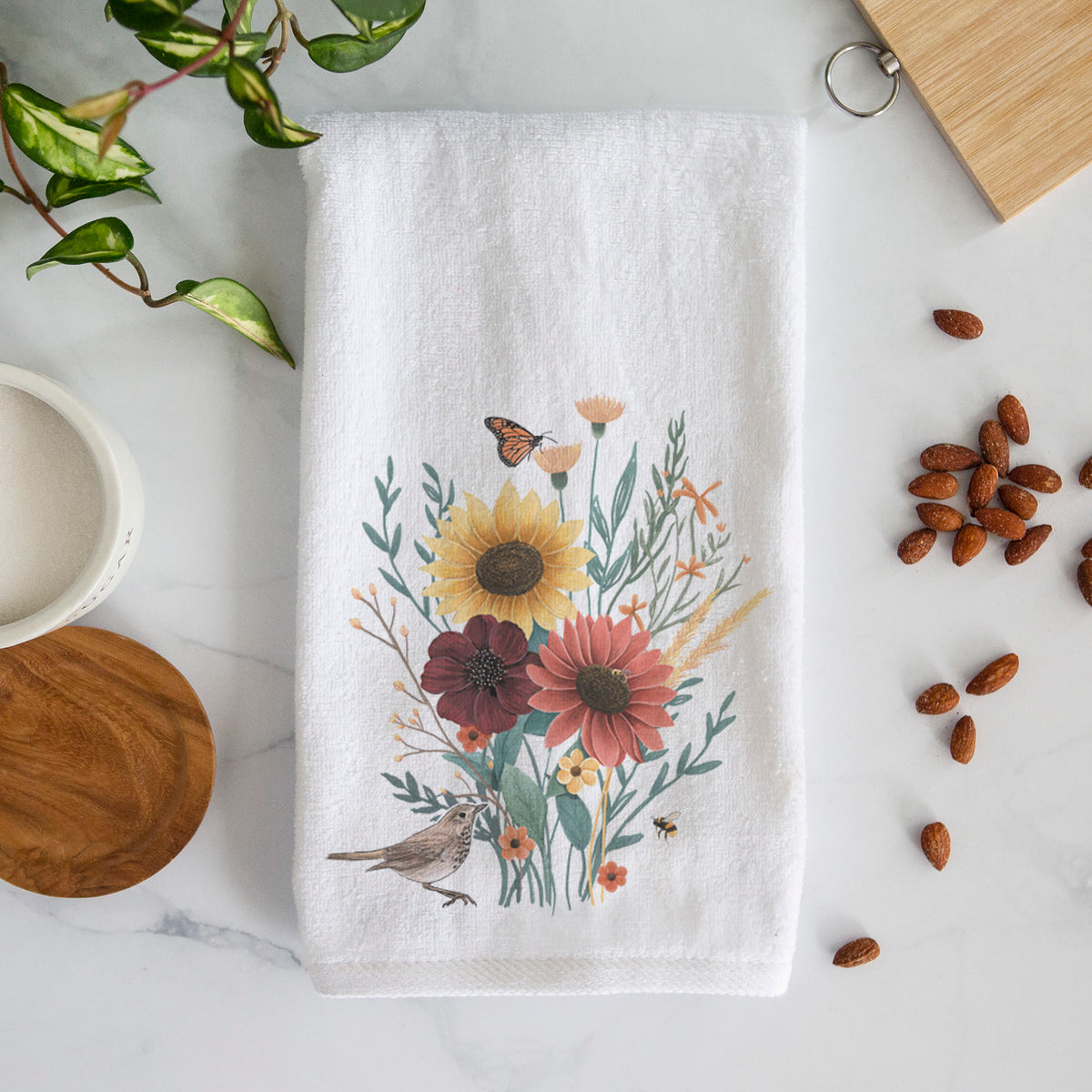 White hand towel printed with a full-color bouquet of sunflowers, red flowers and wildflowers with butterflies and a small bird.