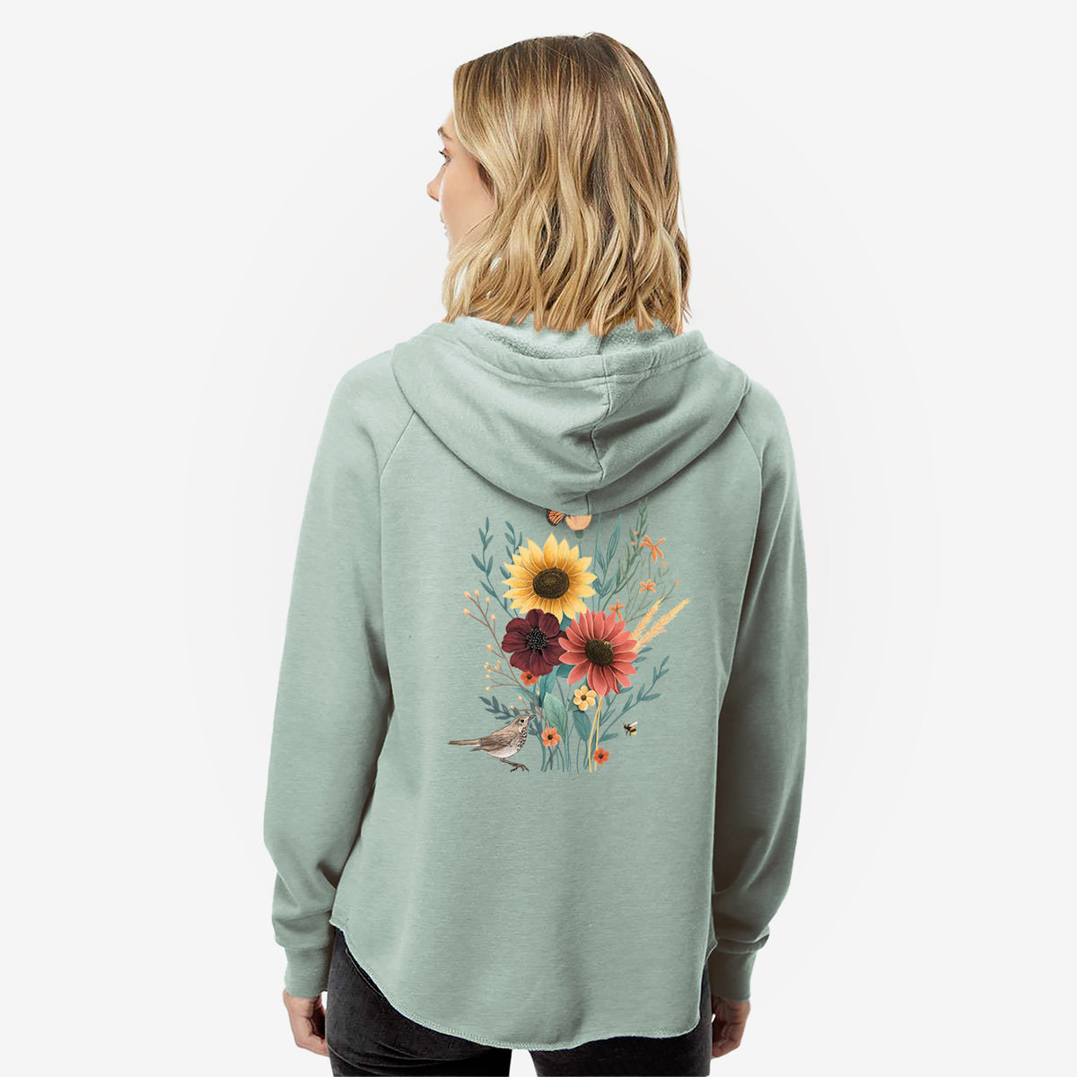 Woman wearing a sage green women's Cali Wave zip-up sweatshirt printed with a full-color bouquet of sunflowers, red flowers and wildflowers with butterflies and a small bird, seen from behind.