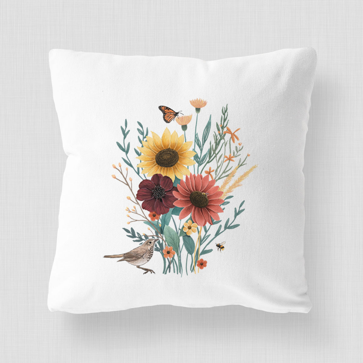 White pillow cover printed with a full-color bouquet of sunflowers, red flowers and wildflowers with butterflies and a small bird.