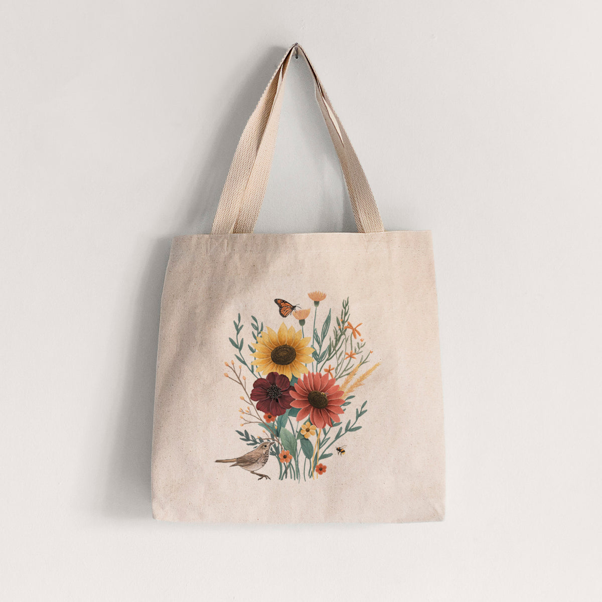 Natural canvas tote bag printed with a full-color bouquet of sunflowers, red flowers and wildflowers with butterflies and a small bird.