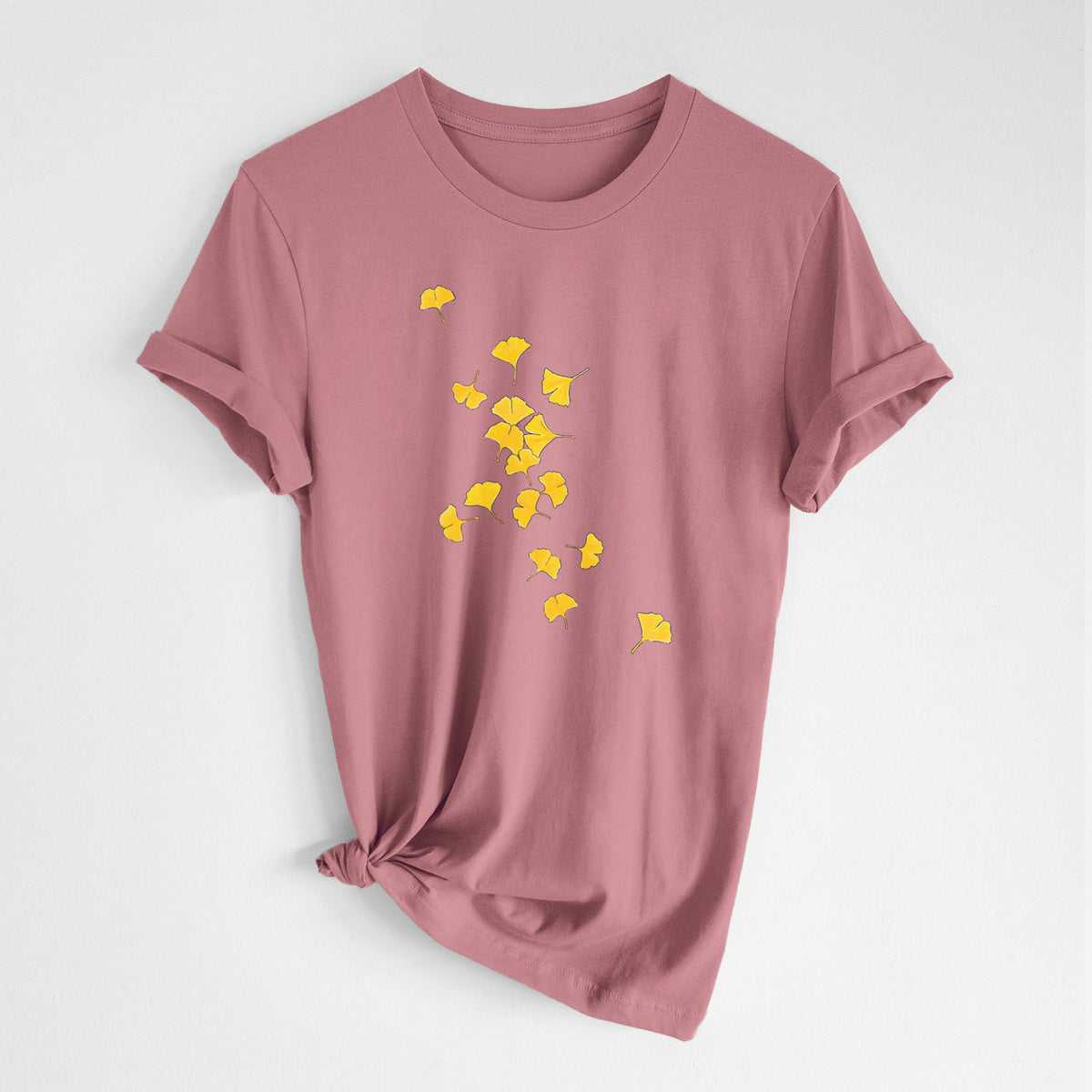 Mauve pink lightweight cotton t-shirt laid flat with the sleeves rolled, printed with a scatter of bright yellow fan-shaped ginkgo leaves falling.