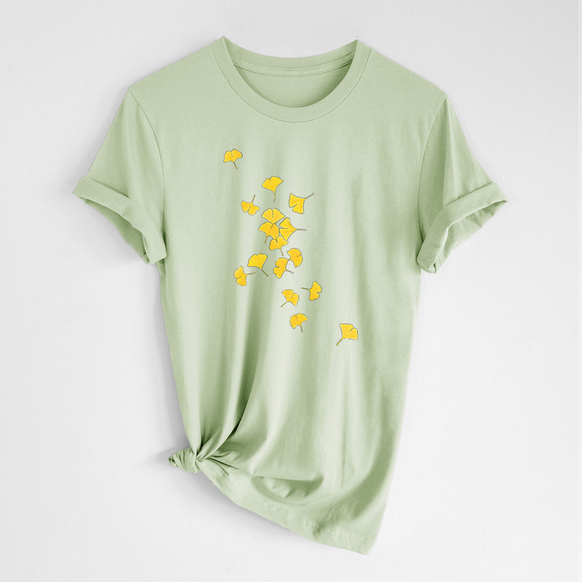 Spring green lightweight cotton t-shirt laid flat with the sleeves rolled, printed with a scatter of bright yellow fan-shaped ginkgo leaves falling.