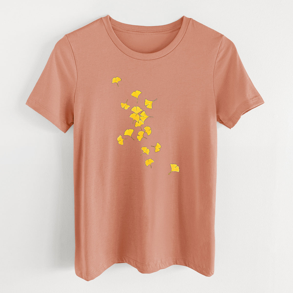 Terracotta orange women's relaxed fit cotton t-shirt laid flat, printed with a scatter of bright yellow fan-shaped ginkgo leaves falling.