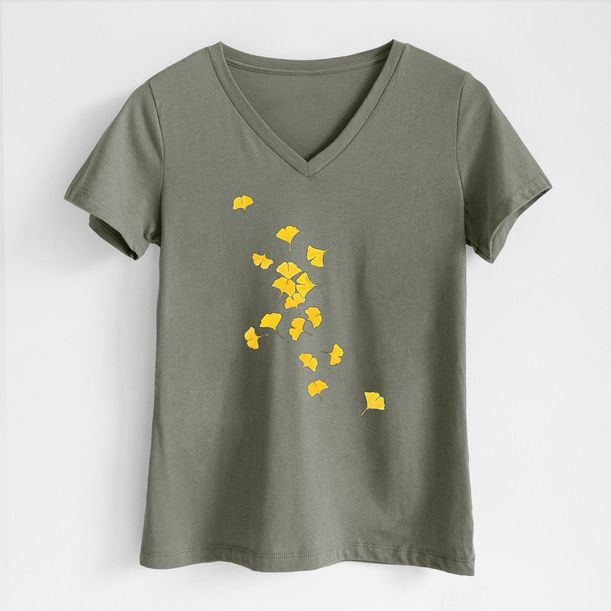 Military green women's relaxed fit cotton V-neck t-shirt laid flat, printed with a scatter of bright yellow fan-shaped ginkgo leaves falling.