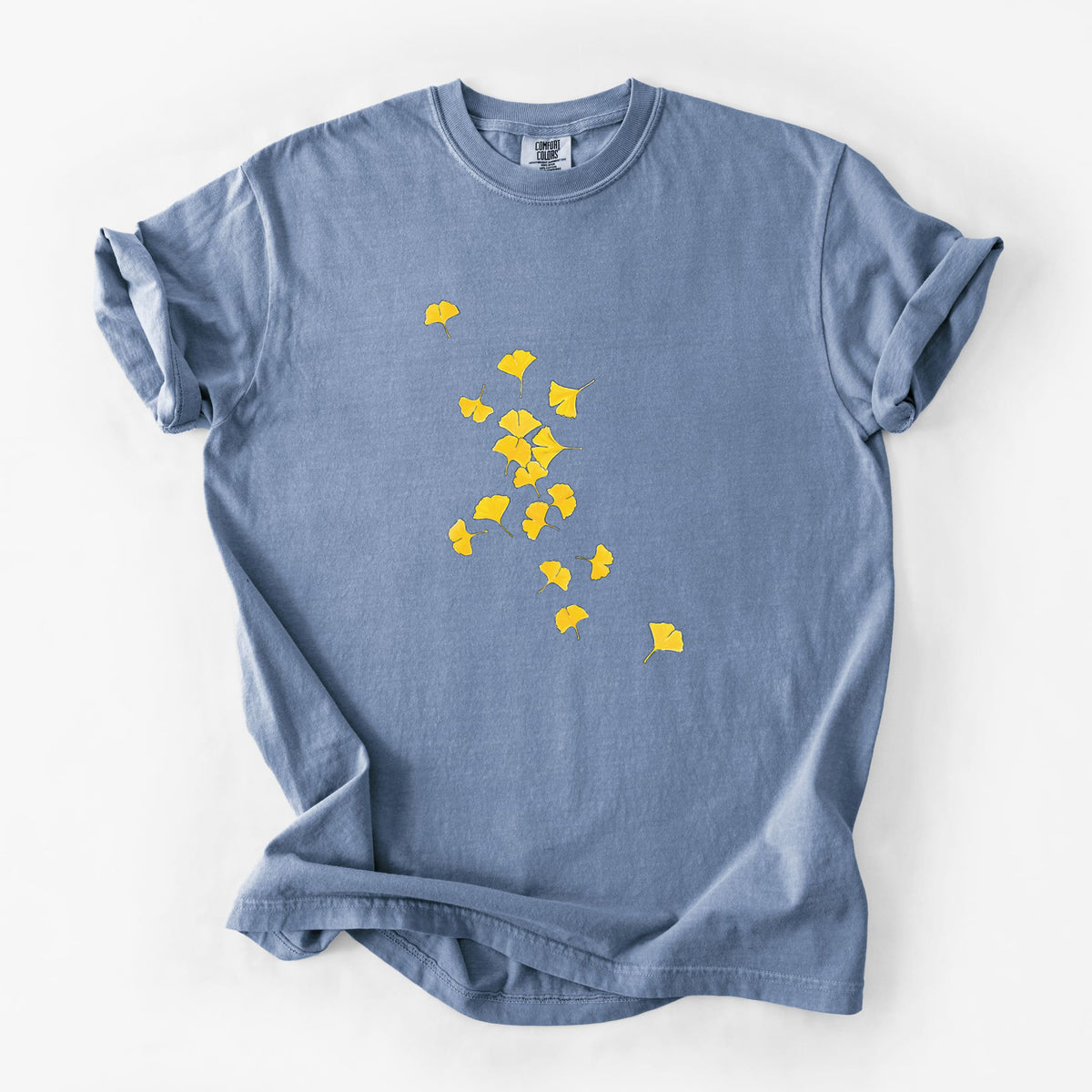 Blue jean Comfort Colors t-shirt laid flat, printed with a scatter of bright yellow fan-shaped ginkgo leaves falling.