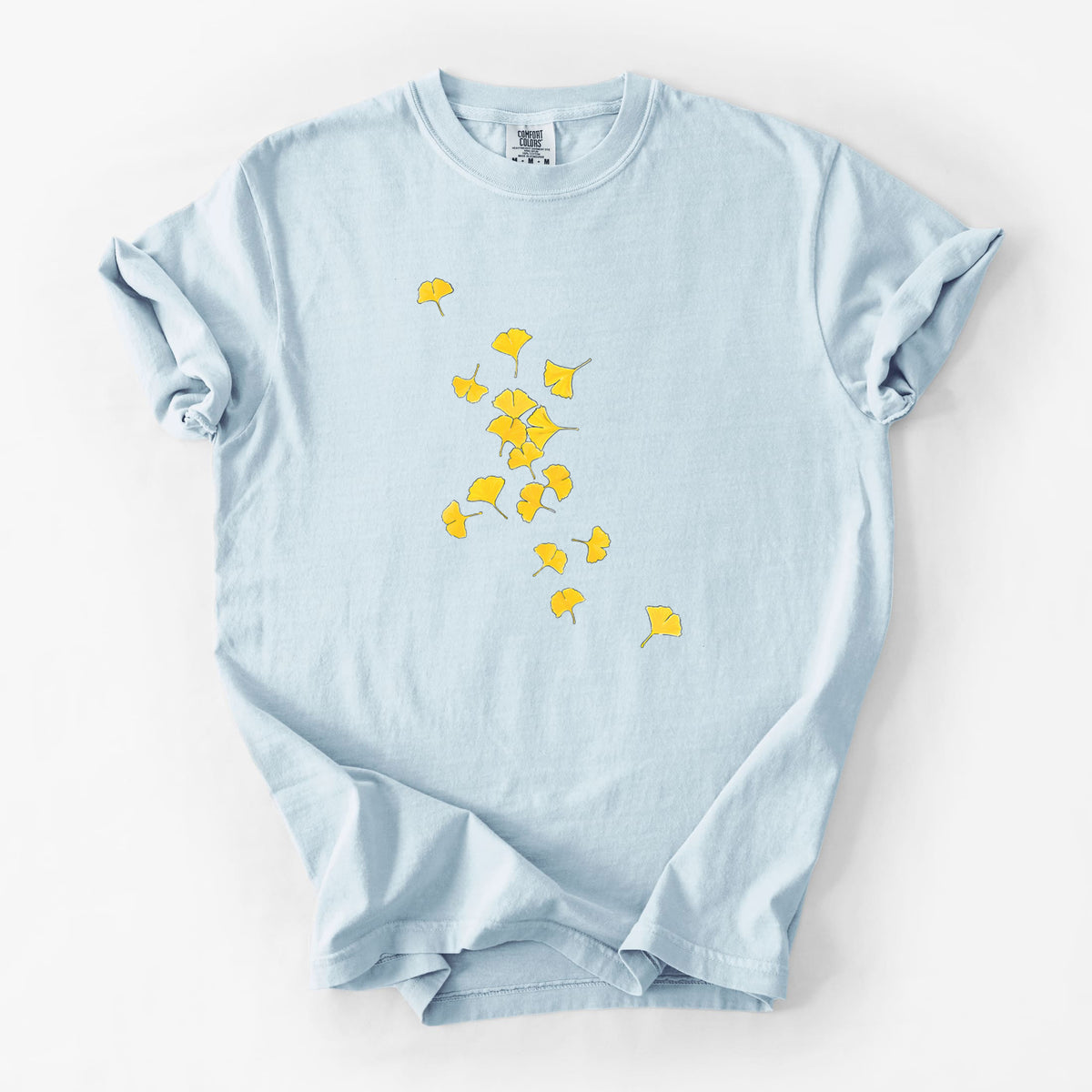 Chambray blue Comfort Colors t-shirt laid flat, printed with a scatter of bright yellow fan-shaped ginkgo leaves falling.