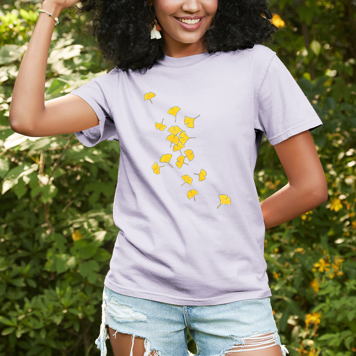 Woman wearing a Comfort Colors t-shirt printed with a scatter of bright yellow fan-shaped ginkgo leaves falling, outdoors.