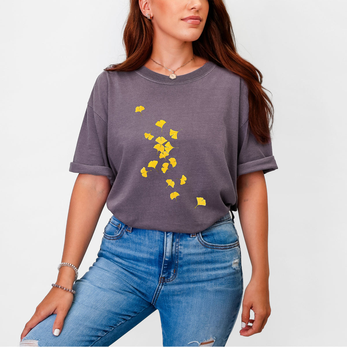 Woman wearing a Comfort Colors t-shirt printed with a scatter of bright yellow fan-shaped ginkgo leaves falling.