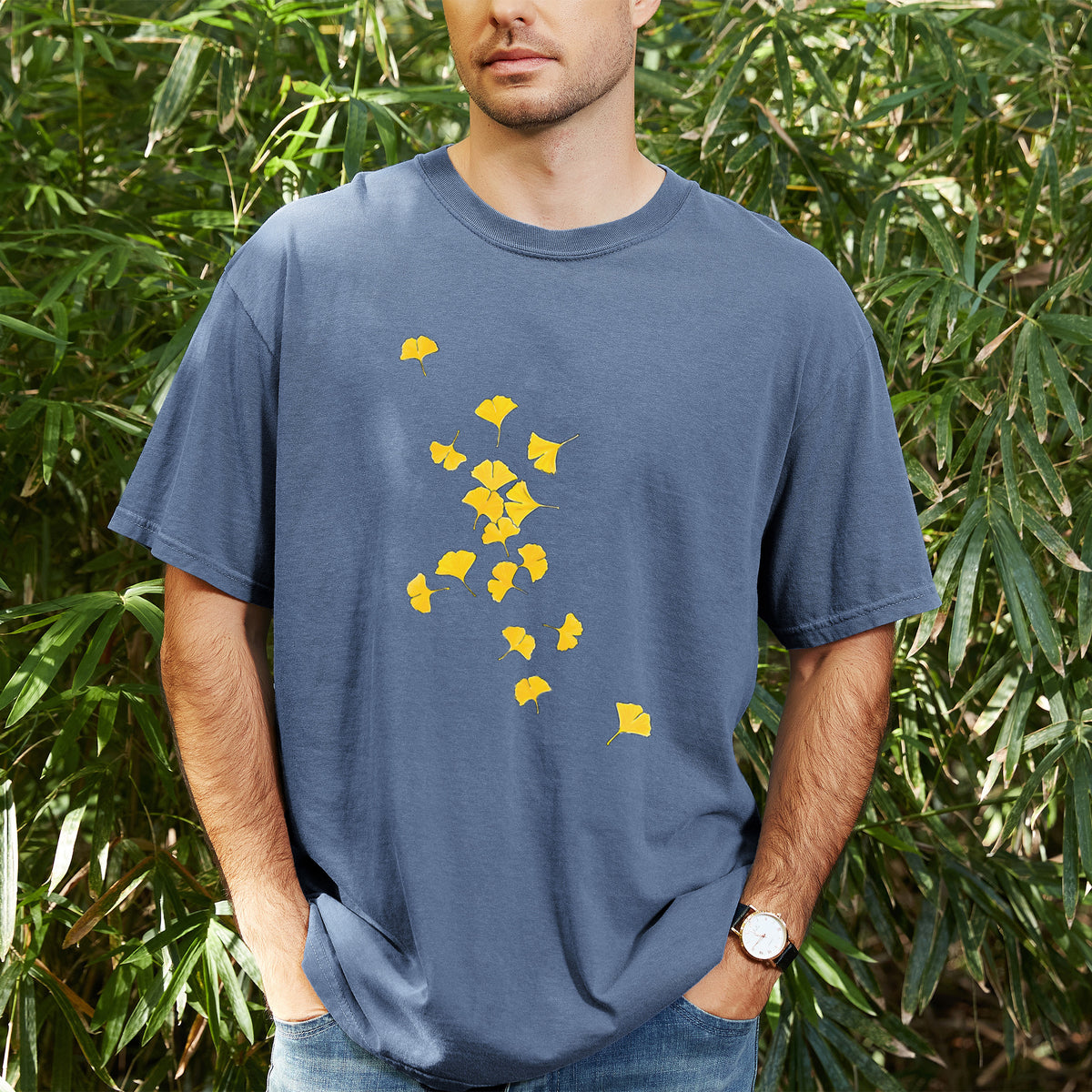Man wearing a Comfort Colors t-shirt printed with a scatter of bright yellow fan-shaped ginkgo leaves falling, outdoors.