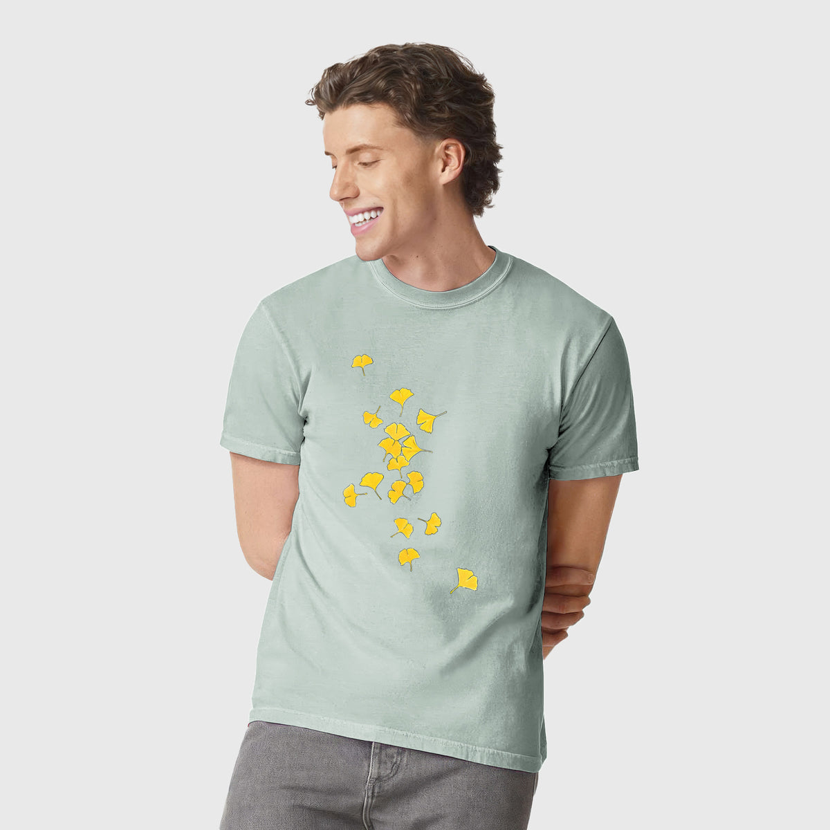 Man wearing a Comfort Colors t-shirt printed with a scatter of bright yellow fan-shaped ginkgo leaves falling.