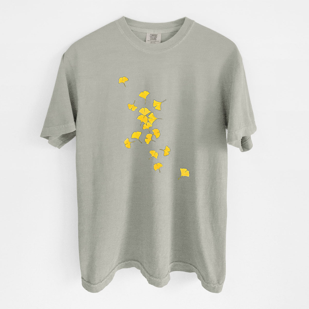 Sandstone beige Comfort Colors t-shirt laid flat, printed with a scatter of bright yellow fan-shaped ginkgo leaves falling.