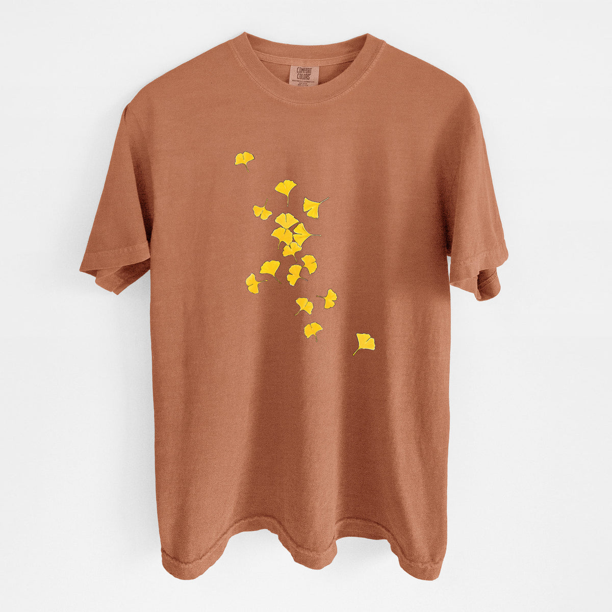 Yam burnt orange Comfort Colors t-shirt laid flat, printed with a scatter of bright yellow fan-shaped ginkgo leaves falling.