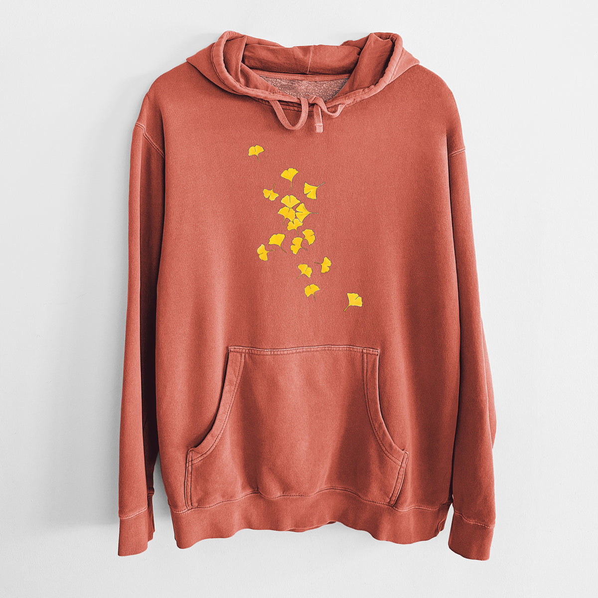 Amber orange pigment dyed hoodie laid flat, printed with a scatter of bright yellow fan-shaped ginkgo leaves falling.