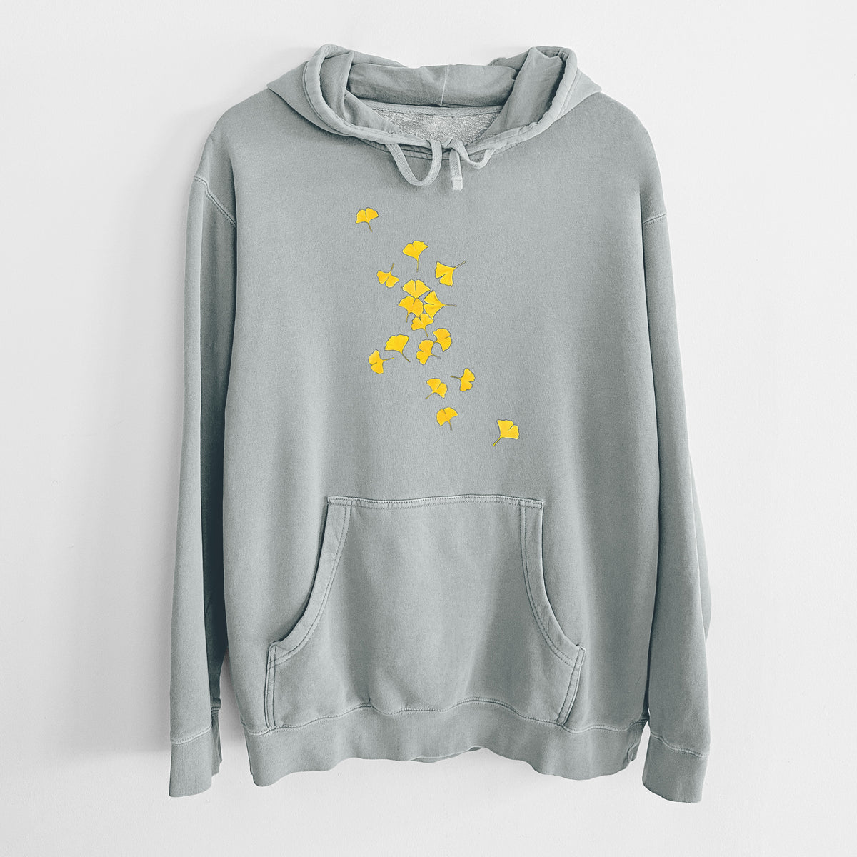 Sage green pigment dyed hoodie laid flat, printed with a scatter of bright yellow fan-shaped ginkgo leaves falling.