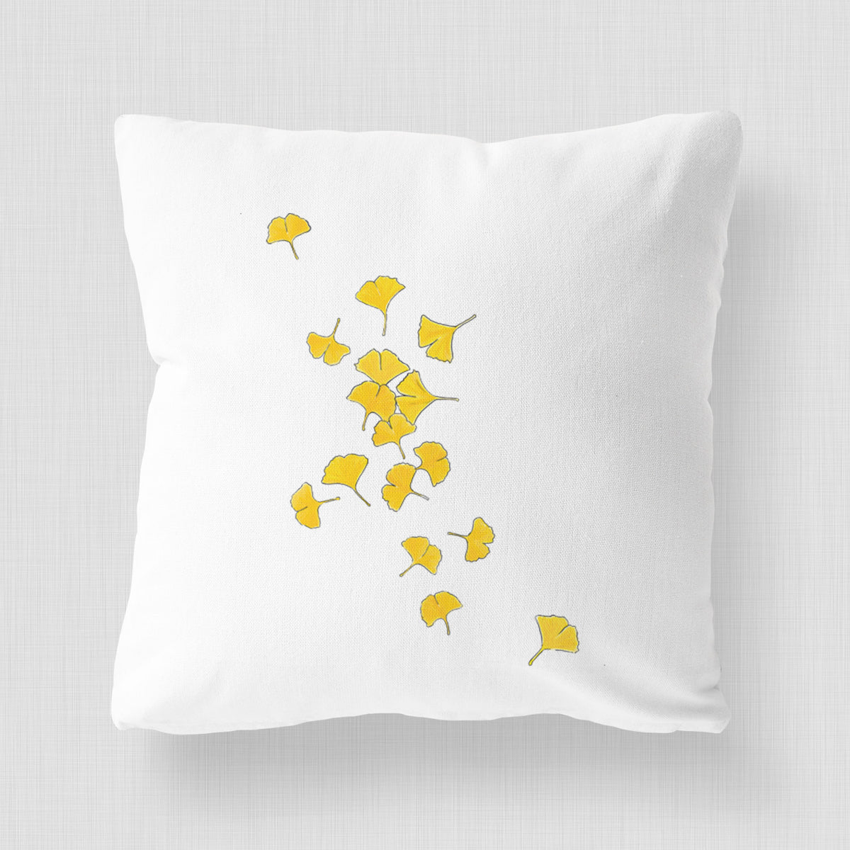 White pillow cover printed with a scatter of bright yellow fan-shaped ginkgo leaves falling.