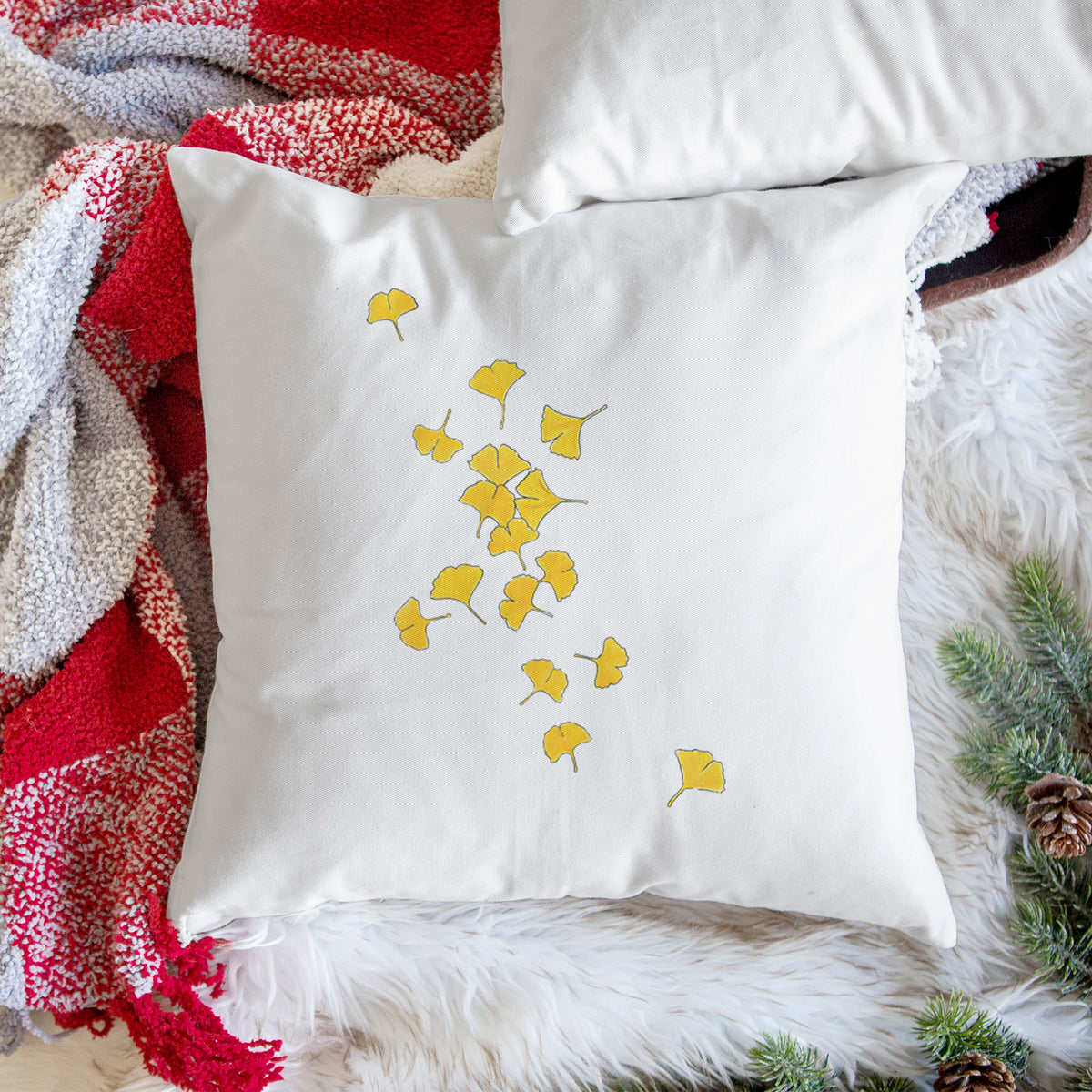 White pillow cover printed with a scatter of bright yellow fan-shaped ginkgo leaves falling, on a woven chair.