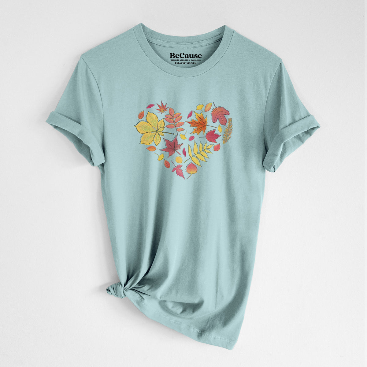 Dusty blue lightweight cotton t-shirt laid flat with the sleeves rolled, printed with a full-color heart shape made of autumn leaves in orange, red and yellow.
