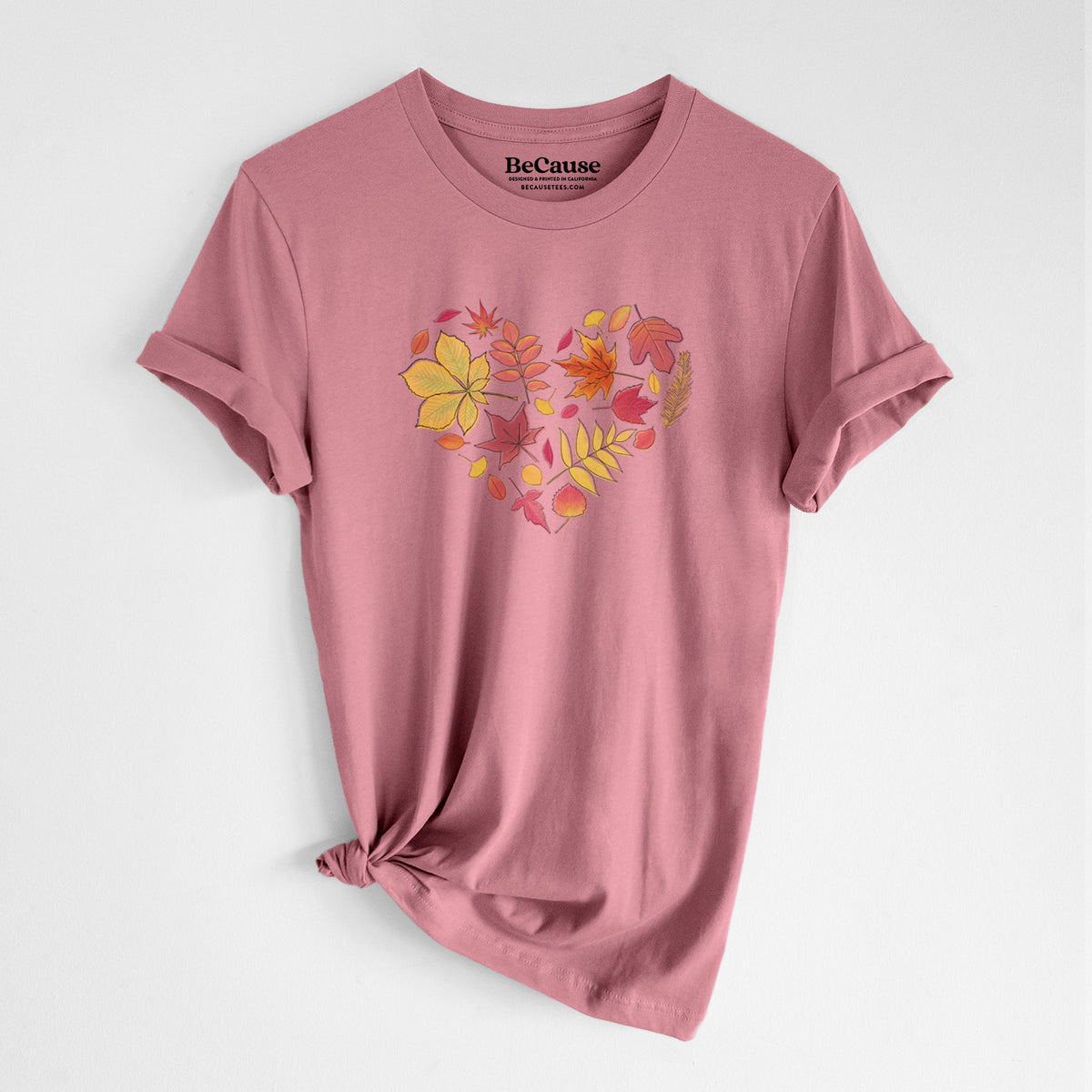 Mauve pink lightweight cotton t-shirt laid flat with the sleeves rolled, printed with a full-color heart shape made of autumn leaves in orange, red and yellow.