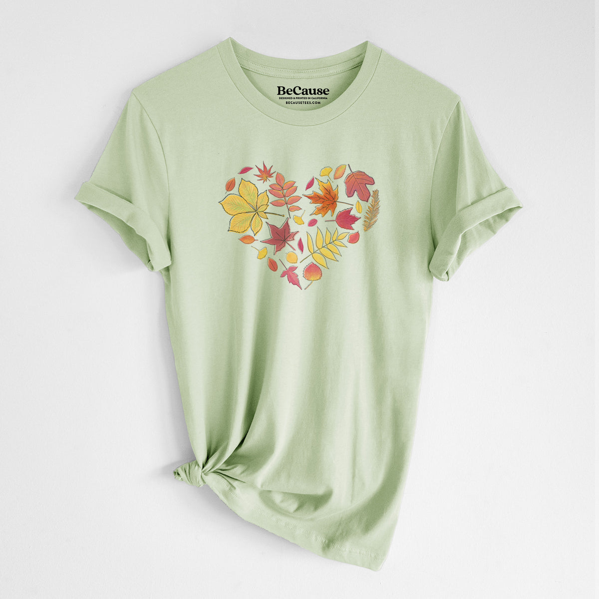 Spring green lightweight cotton t-shirt laid flat with the sleeves rolled, printed with a full-color heart shape made of autumn leaves in orange, red and yellow.